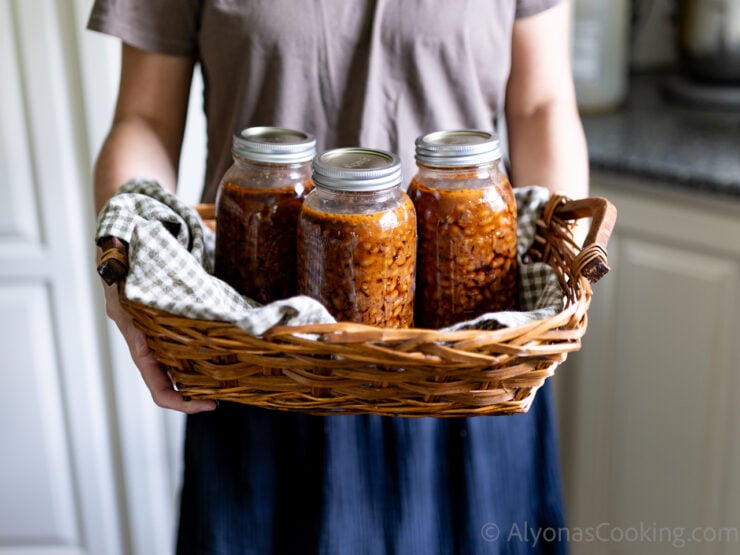 image of Alyona holding a bunch of home-canned baked beans in a basket lined with a gingham towel
