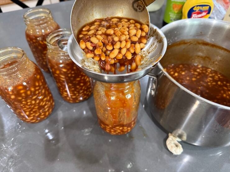 image of prepared baked beans being filled into jars and ready for canning