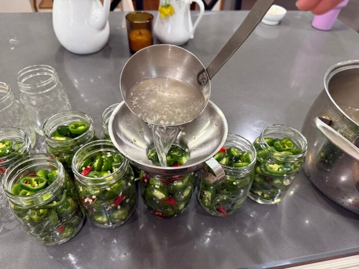 image of packed jalapeños in pint jars being ladled with brine for canning