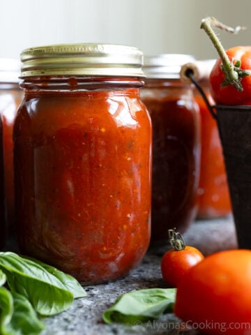 image of home canned pizza sauce by a bucket of fresh tomatoes and fresh basil