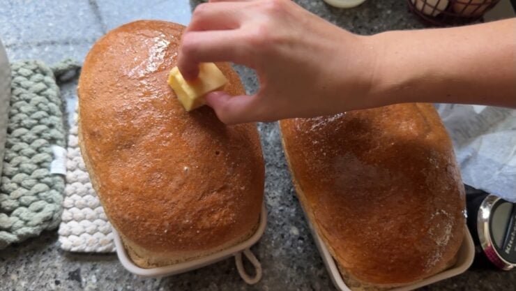 image of Alyona smearing butter on the tops of sourdough sandwich loaves